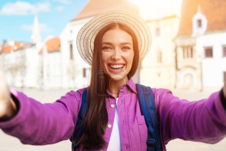 Téléchargez les photos : Un étudiant millénaire aime prendre un selfie tout en explorant les rues historiques dans une ville européenne ensoleillée, en plein air et souriant - en image libre de droit