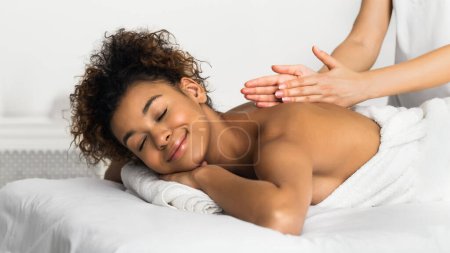 Téléchargez les photos : Dans ce cadre serein, une femme afro-américaine se fait faire un massage spa apaisant administré par un professionnel. L'image représente le calme et la relaxation vécus pendant la thérapie - en image libre de droit
