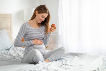A pregnant european lady at home on her bed, contemplating pregnancy while holding a nutritious apple