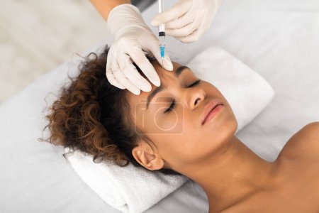 Foto de Una paciente afroamericana joven está recibiendo un tratamiento de inyección cosmética de un profesional de la salud, centrándose en la belleza y el cuidado de la piel - Imagen libre de derechos