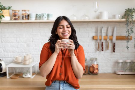 Photo for A muslim arab zoomer woman exudes contentment as she enjoys a warm drink at home, illustrating a moment of peace in a middle eastern household - Royalty Free Image