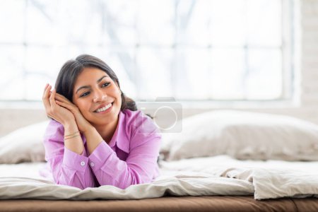 Téléchargez les photos : Une femme musulmane de contenu avec un sourire chaleureux se relaxe sur son lit à la maison, mettant en valeur un sentiment de tranquillité et de confort, espace de copie - en image libre de droit