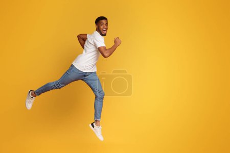 Téléchargez les photos : Homme afro-américain motivé émotionnel courant pour viser en l'air, sautant sur fond orange - en image libre de droit