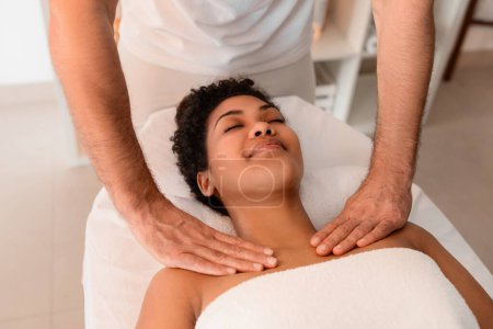 A relaxing scene in a spa setting with African American woman having a neck massage by a professional masseur, promoting wellness and self-care