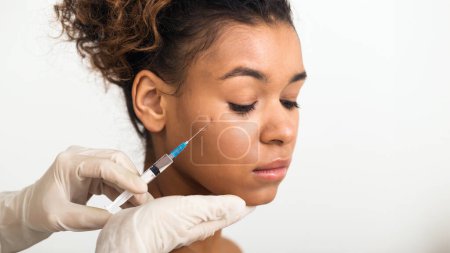 Foto de Un profesional de manos suaves administra una inyección facial a una joven afroamericana, que representa tratamientos avanzados para el cuidado de la piel - Imagen libre de derechos