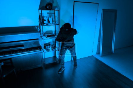 Photo for This photo captures the tension of a night-time burglary with a silent thief ready to steal, lurking in an apartment living room - Royalty Free Image