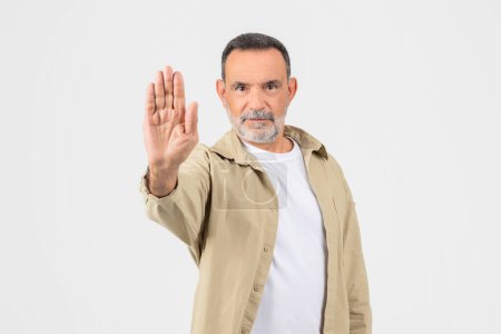 A mature man with a beard, wearing a casual shirt, extends his hand forward in a stopping gesture against a white background