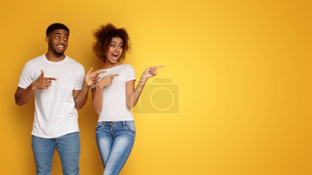 Téléchargez les photos : Wow Excité homme et femme afro-américain souriant et joyeux pointant de côté à l'espace vide sur fond orange - en image libre de droit