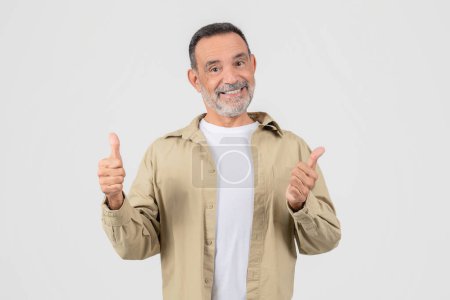 An optimistic senior man gives a thumbs up, expressing approval and positivity, dressed in casual wear, isolated on a white background