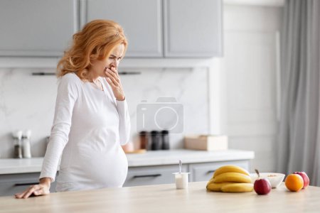 Téléchargez les photos : Moment capturé d'une femme enceinte européenne dans la douleur, berçant son ventre dans un cadre de cuisine, sous-jacent à l'importance de la nutrition - en image libre de droit