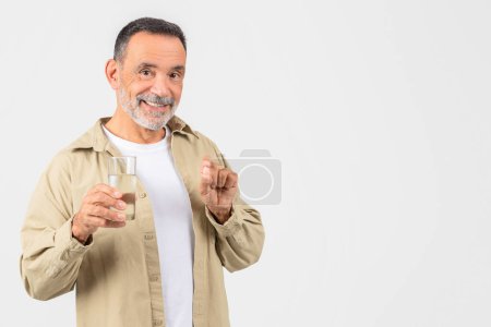 An elderly man holding a glass of water and a pill, isolated on white, promotes health care and responsible medication usage among seniors, copy space