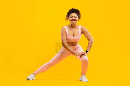 Foto de Mujer afroamericana con una sonrisa radiante realizando estiramientos laterales, promoviendo la aptitud y el bienestar, aislada sobre un fondo amarillo - Imagen libre de derechos