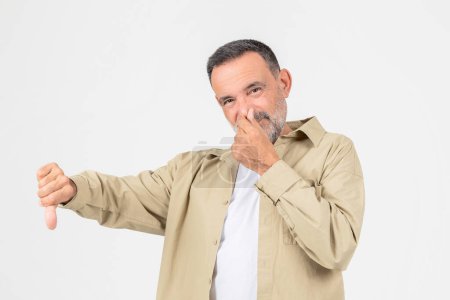 A critical elderly man offers a thumbs down gesture while smirking, isolated on white, expressing disapproval or dissatisfaction
