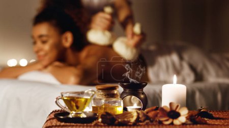 Photo for Woman getting thai herbal compress massage in spa with aroma candles on foreground - Royalty Free Image