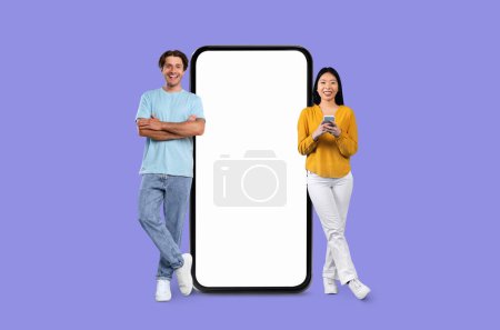 Photo for A happy Multiracial couple stands next to an enormous mobile screen on a purple studio background - Royalty Free Image
