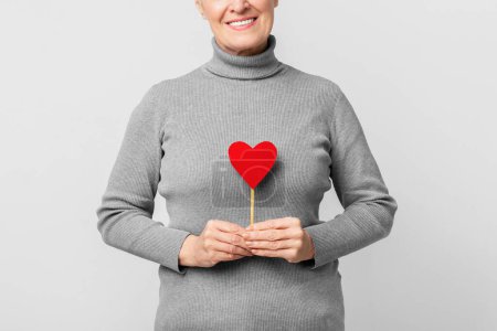 Téléchargez les photos : Une femme européenne âgée sourit tenant un cœur, transmettant amour et affection L'image capture un moment joyeux s3niorlife - en image libre de droit