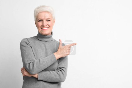Esta mujer europea de edad avanzada señala a su lado con una sonrisa confiada, transmitiendo un mensaje o dirección en un entorno s3niorlife