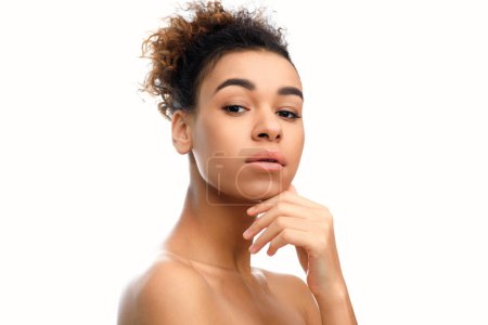 Une femme afro-américaine réfléchie pose la main sur le menton sur un fond blanc, incarnant des thèmes de spa et de bien-être pour l'imagerie de stock