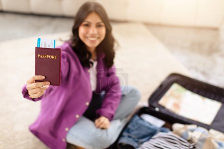 Téléchargez les photos : Une jeune femme rayonnante du Moyen-Orient présente fièrement son passeport et sa carte d'embarquement, symbolisant l'excitation du voyage et de l'aventure - en image libre de droit