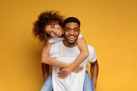 Photo for Happy african-american man and woman having fun together, riding piggyback, orange background - Royalty Free Image