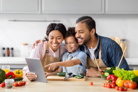 Photo for African American couple with their child using a tablet while cooking in a family kitchen environment - Royalty Free Image