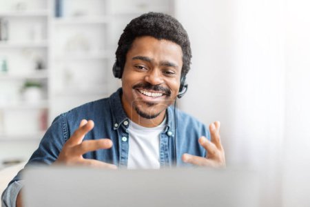 Photo for A joyful African American man wearing a headset is engaging enthusiastically with someone or something on his laptop screen in a bright room - Royalty Free Image