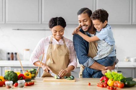 Foto de Amar al padre y al hijo afroamericanos abrazándose en la cocina, reflejando la cercanía familiar mientras preparan la comida juntos - Imagen libre de derechos