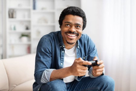 Ein afrikanisch-amerikanischer Mann zeigt ein breites Lächeln, während er einen Spielcontroller in der Hand hält und das Spielen zu Hause genießt