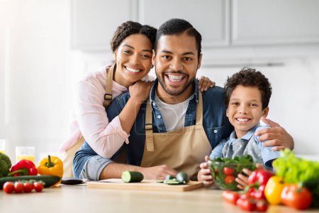 Familia afroamericana cálida sonriendo y cocinando alimentos saludables juntos en una cocina, creando recuerdos