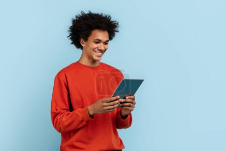 Téléchargez les photos : Un homme afro-américain concentré engagé avec une tablette numérique, isolé sur un fond bleu, représentant la connectivité moderne - en image libre de droit