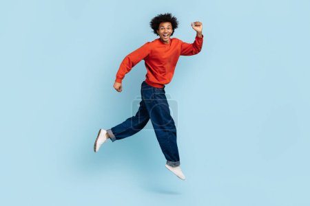 Téléchargez les photos : Un jeune homme afro-américain aux cheveux touffus semble courir joyeusement, représentant la liberté et le bonheur, sur un fond bleu isolé - en image libre de droit