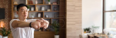 Foto de Hombre asiático maduro estirando las manos, haciendo ejercicio en casa en el interior de la sala de estar, panorama con espacio de copia. chico coreano de mediana edad calentando para el entrenamiento doméstico - Imagen libre de derechos
