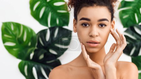 Mujer afroamericana introspectiva con una expresión serena, rodeada de hojas verdes que sugieren un tema de spa y bienestar holístico