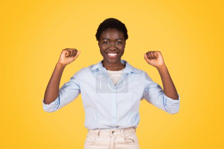 Foto de Mujer negra enérgica levanta las manos en victoria, encapsulando el espíritu triunfante asociado con la General Z Aislada sobre un radiante telón de fondo amarillo - Imagen libre de derechos