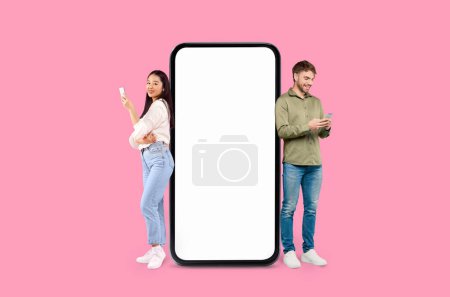 Téléchargez les photos : Un homme et une femme sont debout à côté d'un écran de smartphone surdimensionné sur un fond rose, espace de copie maquette - en image libre de droit