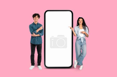 Téléchargez les photos : Jeune homme et femme debout à côté d'un grand écran vertical vierge smartphone sur un fond rose - en image libre de droit