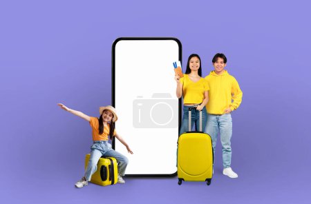 Photo for Happy asian family with luggage beside a large smartphone display conveying the idea of digital travel application technology, isolated on a purple backdrop - Royalty Free Image