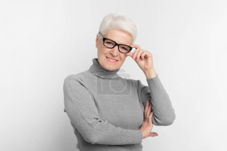 Elderly European woman wearing glasses on grey studio background, exemplifying intelligence for s3niorlife