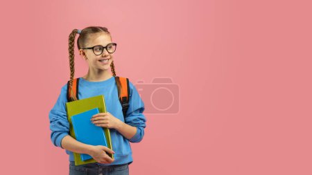 Photo for A cheerful teen girl stands isolated on a pink background holding textbooks, depicting a motivated youngster ready for school, copy space - Royalty Free Image