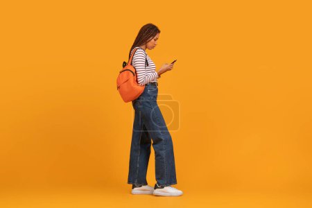 Serene young black woman strolls with a modern vibe, displaying international appeal and multiethnic fashion trends isolated on orange background