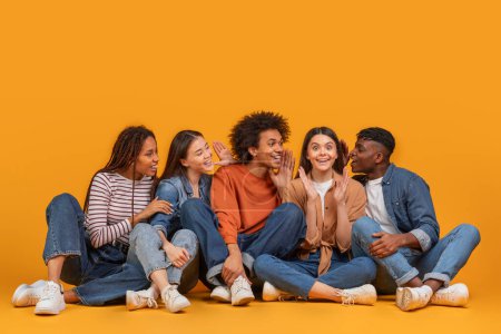 Junge internationale Freunde teilen Flüstern und Lächeln und fangen einen Moment der Freundschaft in einem multirassischen, multiethnischen Szenario ein, isoliert auf gelbem Hintergrund