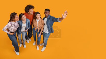 Eine Gruppe fröhlicher multiethnischer Freunde macht beim Gehen ein Selfie und fängt einen Moment der Freude in einem zeitgenössischen Rahmen ein, isoliert auf gelbem Hintergrund, Kopierraum