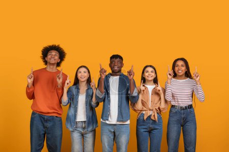 Téléchargez les photos : Cinq individus souriants et pointant vers le haut, debout sur un fond orange, représentant la positivité et le travail d'équipe - en image libre de droit