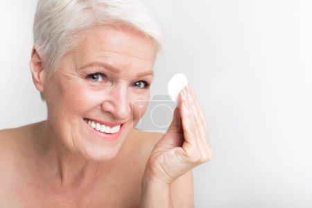 Téléchargez les photos : Femme européenne âgée présente un coton tout en souriant, reflétant l'hygiène et les moments joyeux de s3niorlife - en image libre de droit
