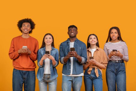 Ein vielfältiges internationales Team junger Freunde, die mit ihren Mobiltelefonen beschäftigt sind, repräsentiert eine multiethnische, multirassische Generation, isoliert auf orangefarbenem Hintergrund