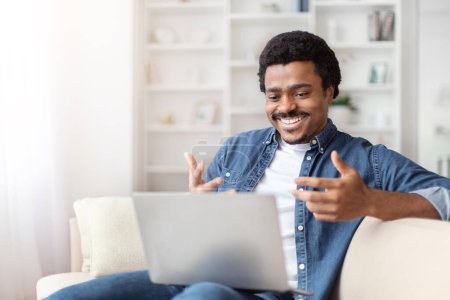 Téléchargez les photos : Un noir afro-américain est vu rire joyeusement lors d'un appel vidéo à la maison, interagissant avec un homme sur son ordinateur portable - en image libre de droit