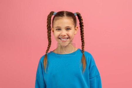 Photo for A cheerful teen girl with long braided pigtails smiling at the camera, isolated on a pink background, showcasing a caucasian youngsters happiness - Royalty Free Image