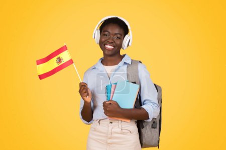 Energetic black woman smiles brightly, holding a Spanish flag to represent her interest in global cultures, key to the zoomer mindset Isolated on yellow