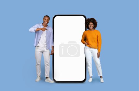 Téléchargez les photos : Homme et femme afro-américain souriant présentant une maquette d'un grand smartphone avec un écran clair - en image libre de droit