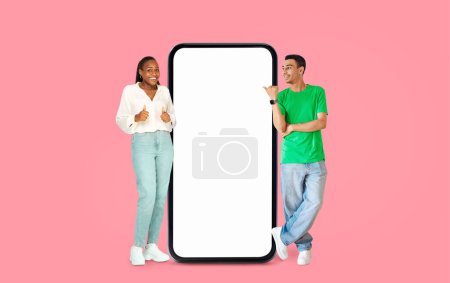 Téléchargez les photos : Afro-Américain donnant les pouces vers le haut et femme souriant à côté d'un écran vide sur un fond rose, idéal pour les publicités - en image libre de droit